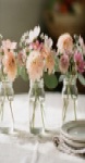 Three small pastel centerpieces in glass jars on a pale linen table